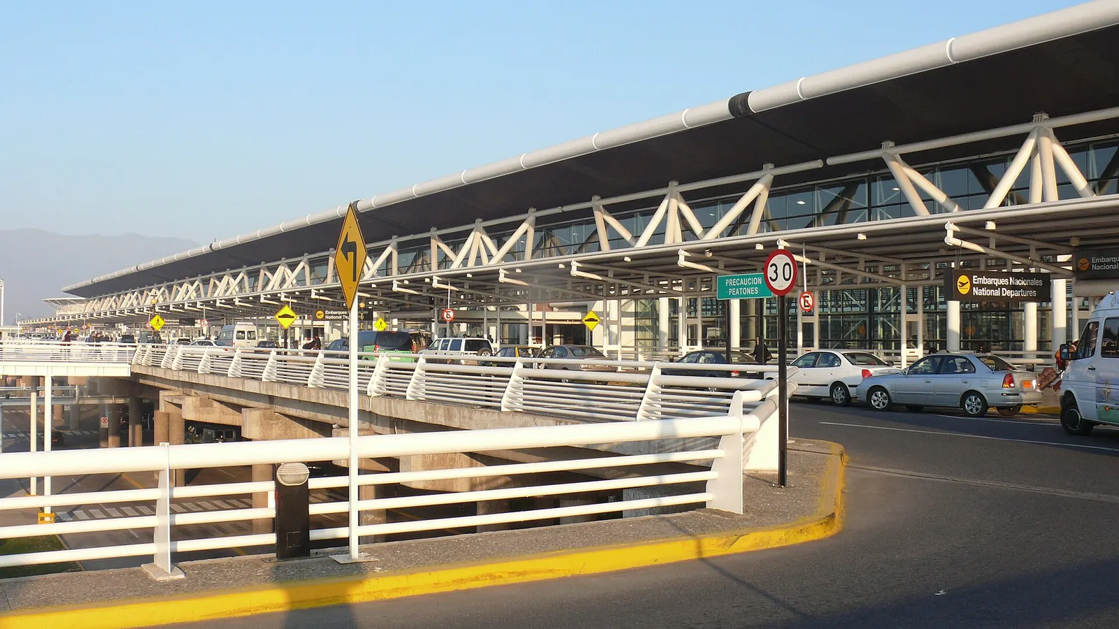 Acceso vehicular elevado del terminal del Aeropuerto Internacional de Santiago, con su estructura de techo metálico y señalética de embarques nacionales.