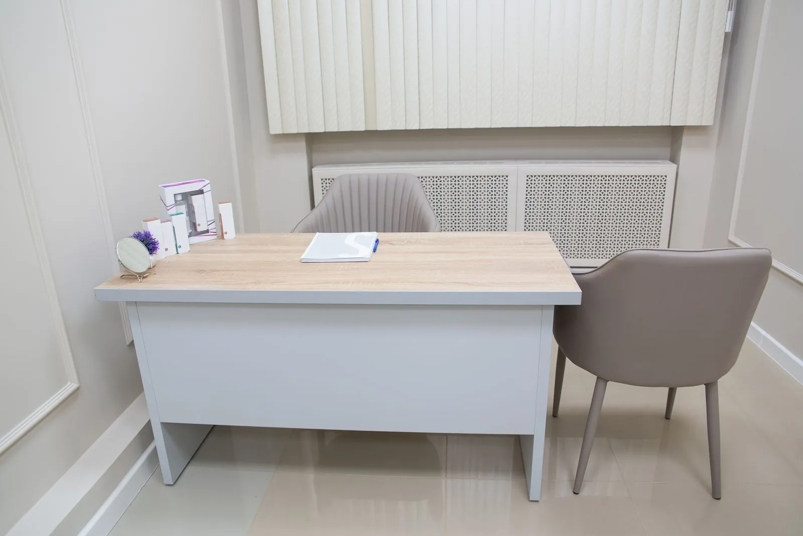 Consulta médica vacía con escritorio, sillas y equipamiento sanitario.