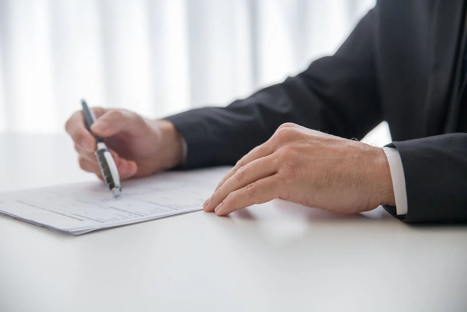 Mano que firma documentos sobre una mesa de trabajo.