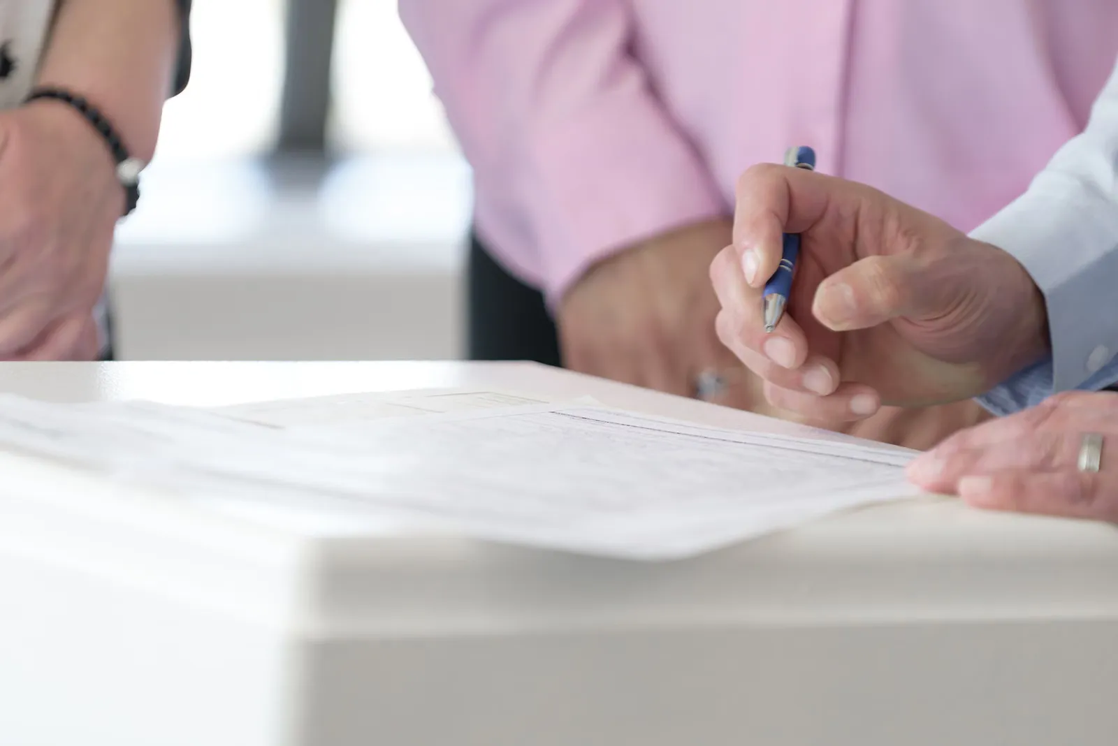 Manos escriben y revisan documentos de oficina sobre una mesa.
