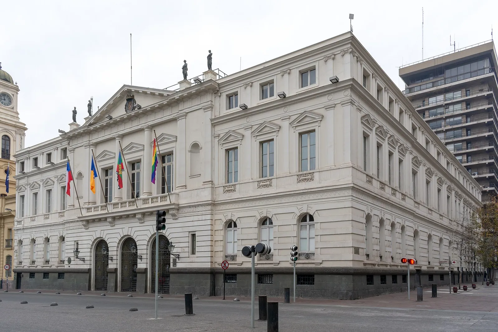 Fachada del edificio de la Municipalidad de Santiago, en la Plaza de Armas de Santiago, con banderas en el balcón y un edificio en altura al costado.