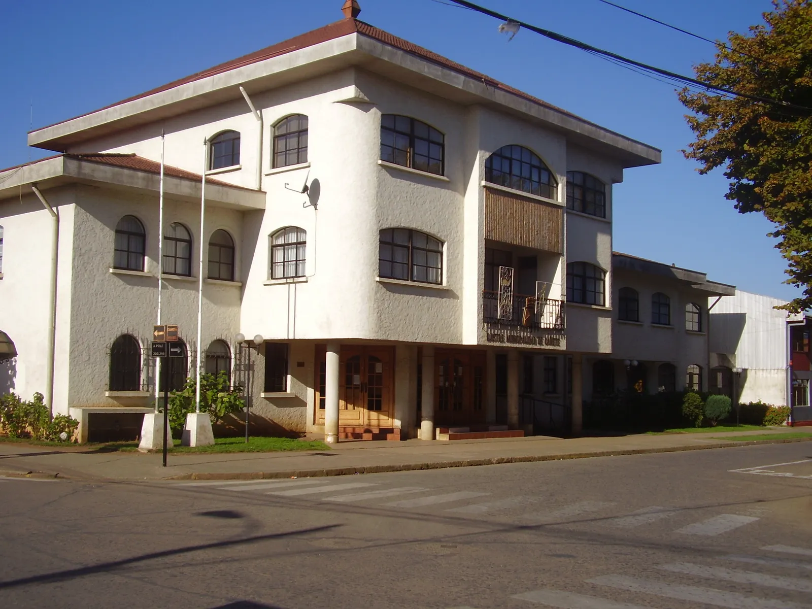 Edificio de la Municipalidad de Cañete: fachada blanca de dos y tres pisos con ventanas en arco y techo de tejas rojas, en una esquina con paso peatonal y cielo despejado.