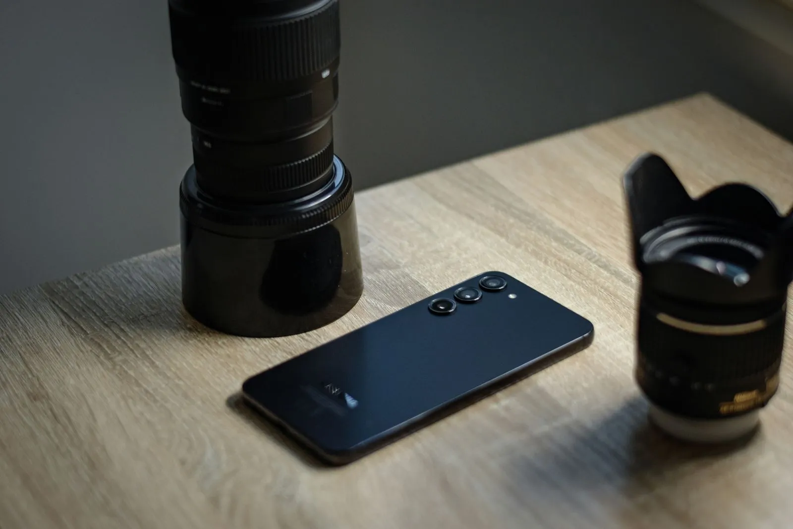 Teléfono inteligente y lentes fotográficos sobre una mesa de madera.