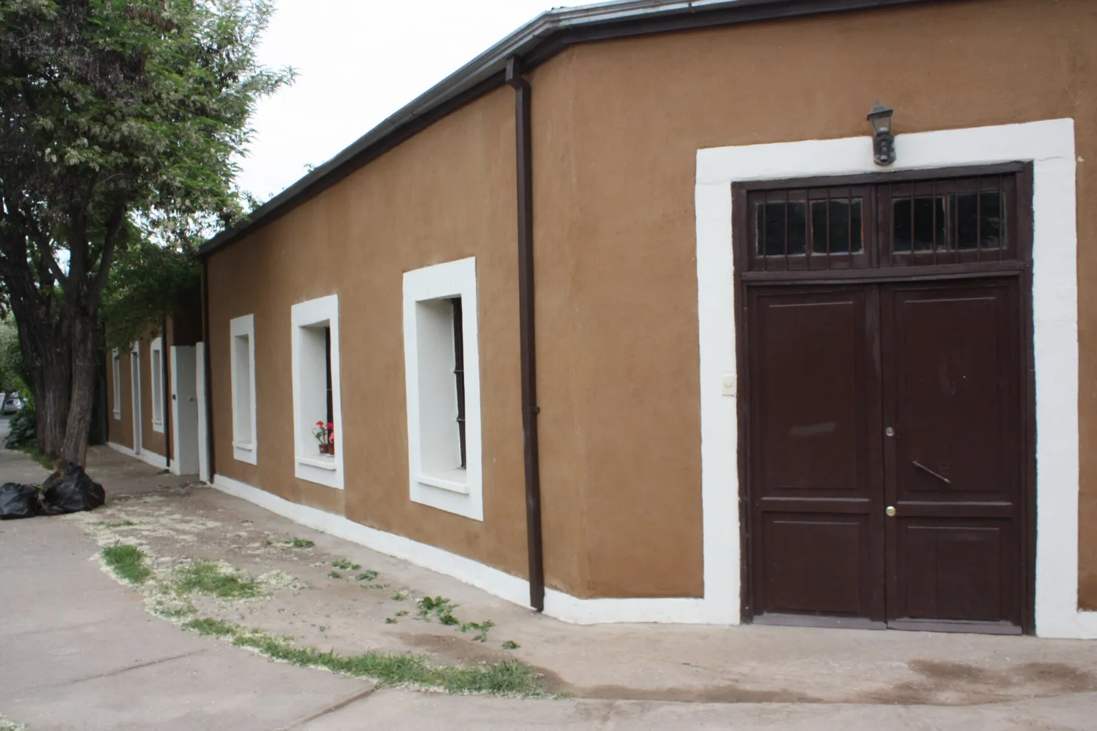 Casa de adobe rehabilitada en la calle Itata, Ñuñoa, con muros color café, ventanas de marco blanco y un portón de madera.