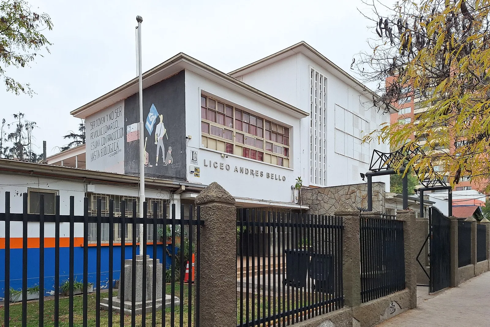 Fachada del Liceo Andrés Bello, en San Miguel, Santiago, tras una reja metálica, con un mural pintado en el muro lateral.