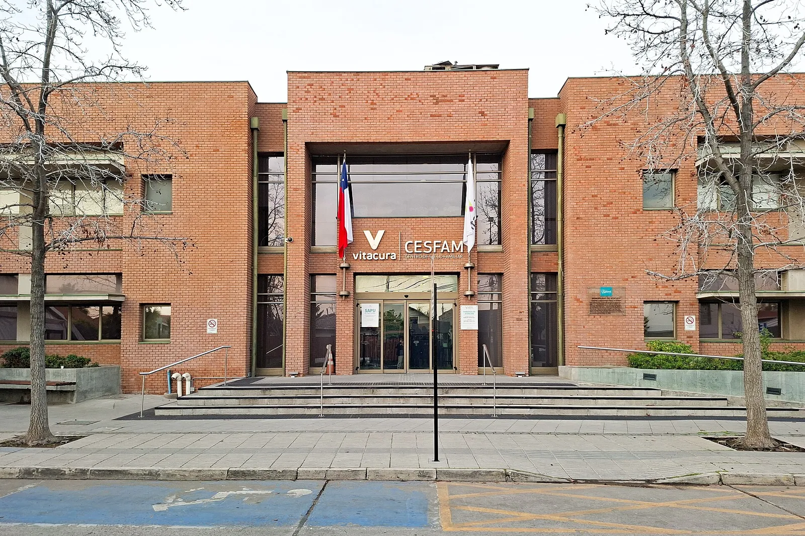 Fachada de ladrillo del Cesfam Vitacura, en Vitacura, Santiago, con banderas en la entrada y escalinata de acceso.