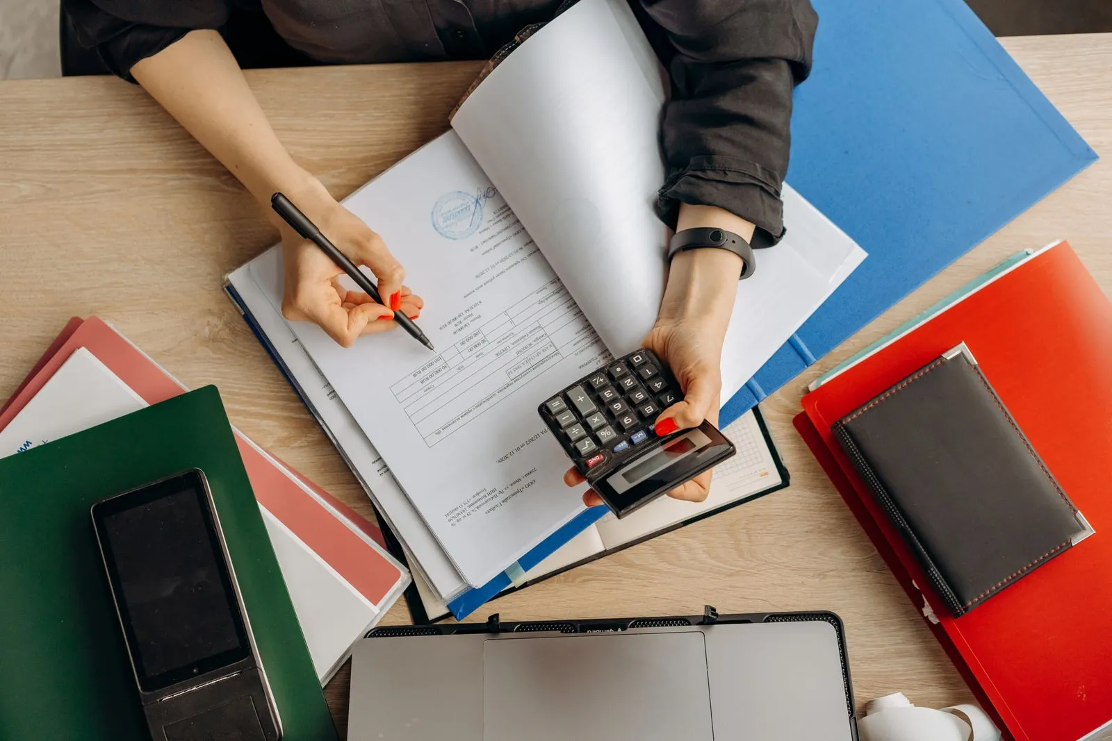 Manos que examinan documentos de contabilidad junto a una calculadora.
