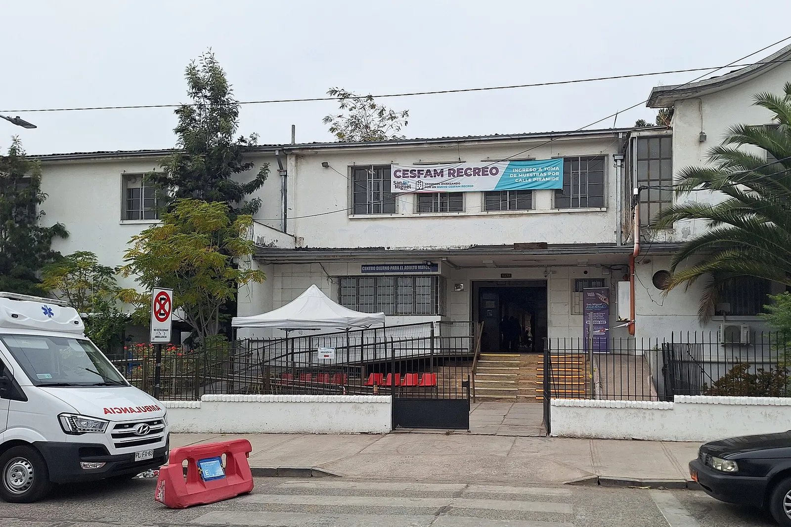 Fachada del Cesfam Recreo, en San Miguel, Santiago, con una ambulancia estacionada a la izquierda y una escalinata de acceso.