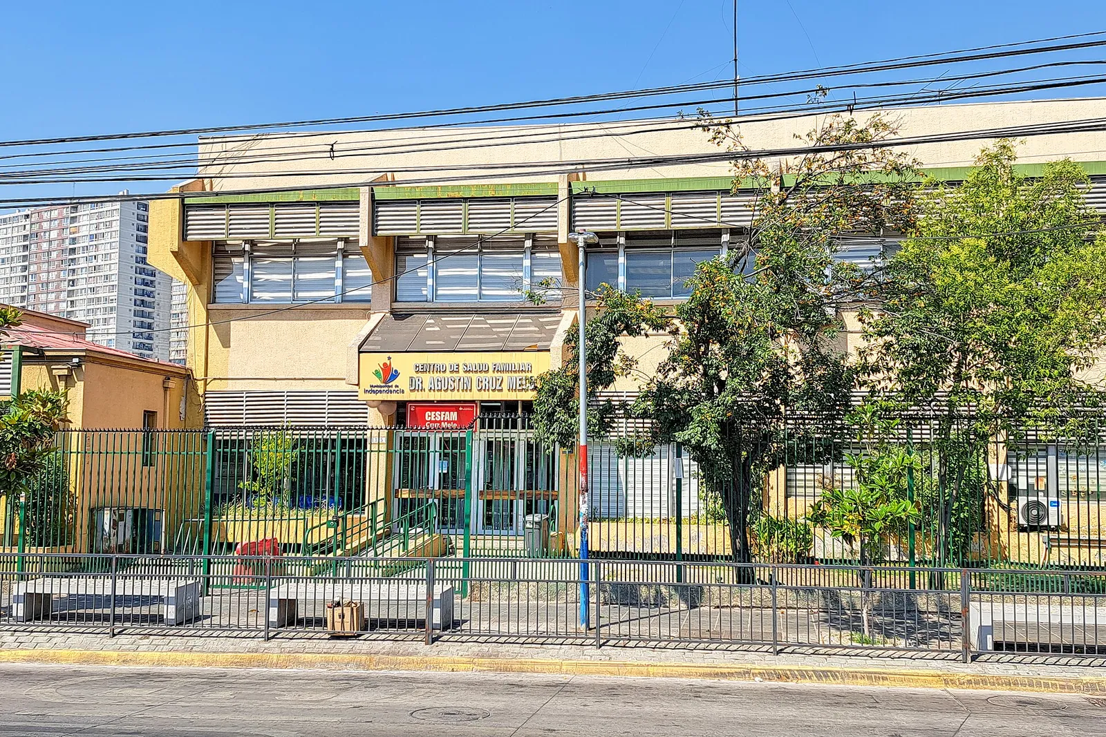 Fachada del Cesfam Dr. Agustín Cruz Melo, en Independencia, Santiago, tras una reja verde y bajo cables del tendido eléctrico.