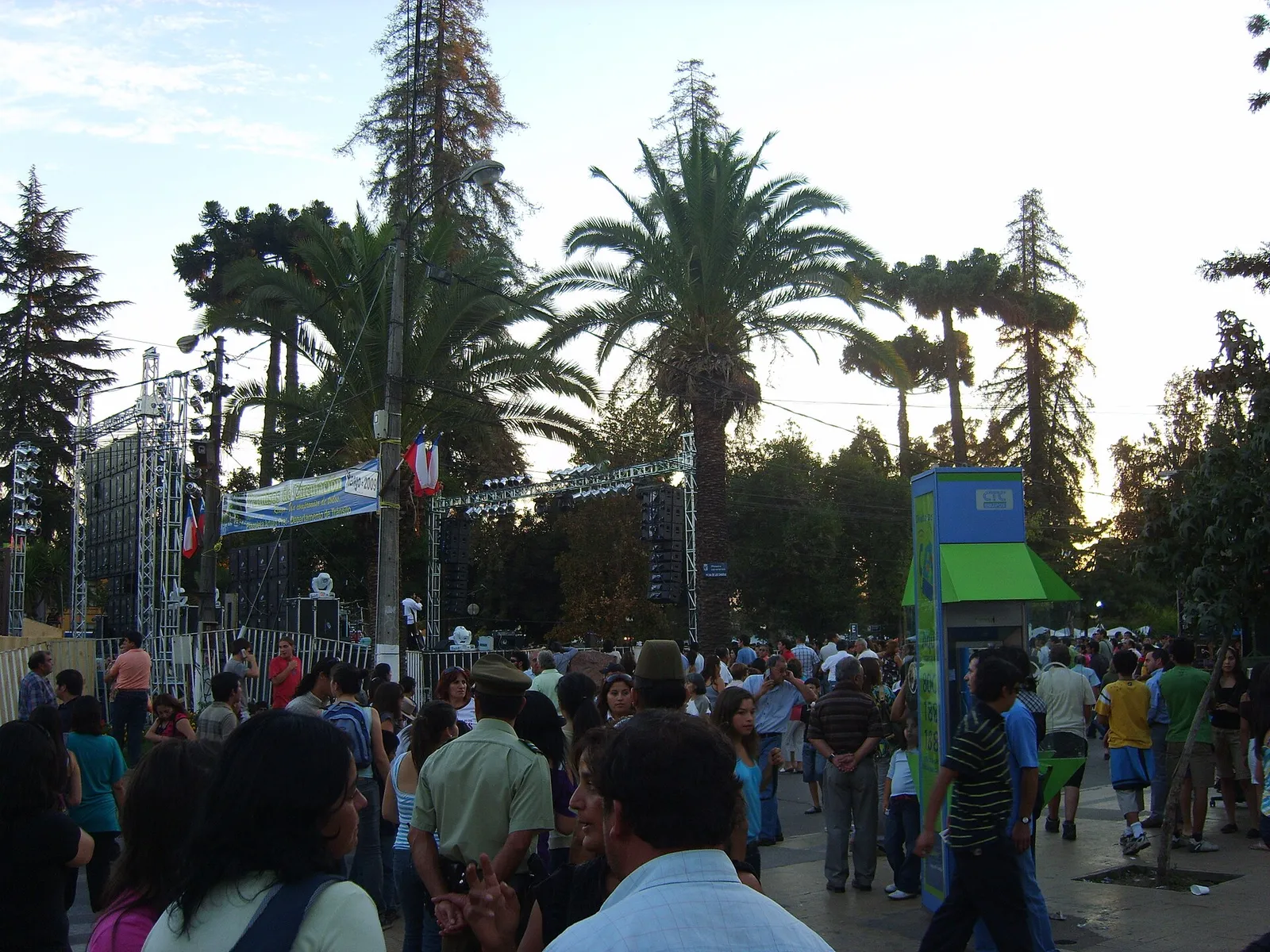 Público en la Fiesta de la Vendimia de Rengo, en su Plaza de Armas, con palmeras, un escenario al fondo y stands.